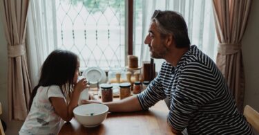 Father and daughter at kitchen table with a breakfast bowl