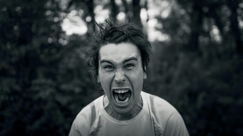 Black and white photo of a man shouting while looking at the camera